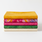 Five coordinating Expressions Batiks fabrics by Riley Blake Designs in a neat folded stack – Curry rich curry yellow on top, with Bouquet multicolor golden orange and pink, hot pink, jungle green, and warm cream tonal batiks below – 100% cotton