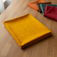 Expressions Batiks Hand-Dyes Curry fabric by Riley Blake Designs folded on a warm wood surface with coordinating warm orange, deep teal, earthy brown, and rich red tonal batik swatches nearby – rich deeply saturated curry yellow hand-dyed batik with warm golden tones, a bold tonal blender perfect for autumn and jewel-tone quilts, 100% cotton batik