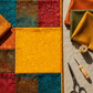 Autumn quilt flat lay featuring Expressions Batiks Hand-Dyes Curry by Riley Blake Designs as the focal fabric – rich deeply saturated curry yellow hand-dyed batik with warm golden tones in pieced blocks with coordinating warm orange, deep teal, earthy brown, and crimson red tonal batiks, folded fabric swatches on a warm linen surface