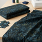 Color Play Mottled Rainstorm fabric by Riley Blake Designs, folded and draped across a sewing table with matching remnants, thread spools, a pincushion, and a sewing machine.