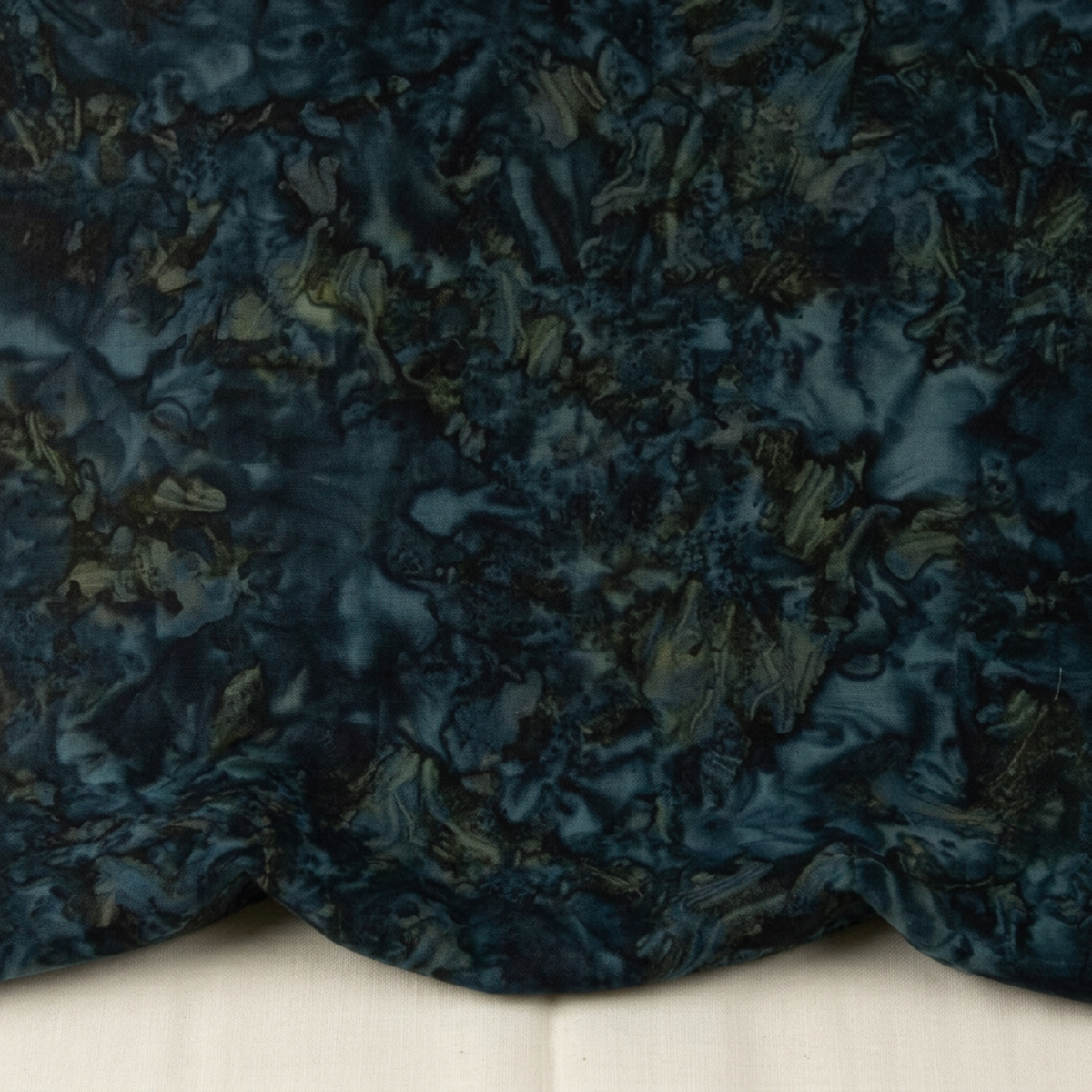 Close-up of Color Play Mottled Rainstorm fabric by Riley Blake Designs, softly draped on a light surface to show its dark blue-teal and olive mottled texture.