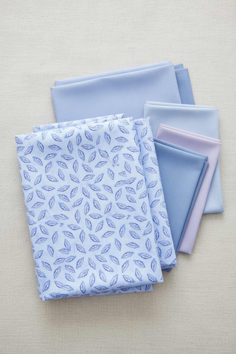 Daydreams Blue Tonal Leaves fabric by Jason Yenter for In The Beginning Fabrics folded on a linen surface – delicate ditsy leaves in soft periwinkle and lavender on dreamy cornflower blue watercolor ground, perfect for spring and blender quilt projects, digitally printed, 100% cotton, 3 yard cut