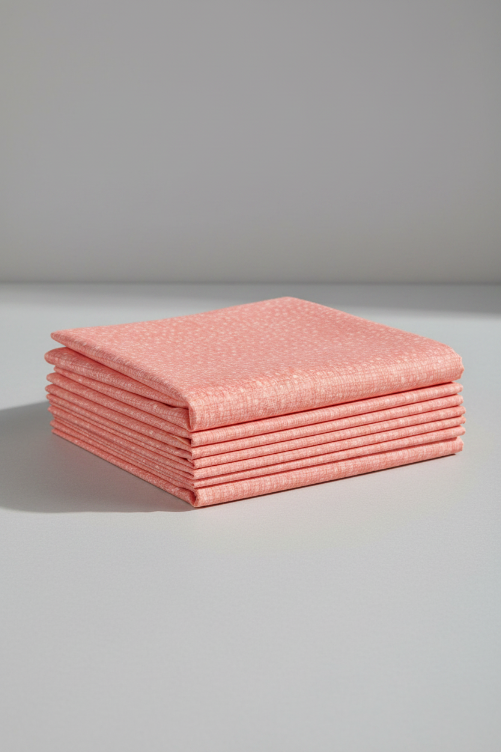 Dotty Thatched Carnation quilting cotton by Robin Pickens for Moda Fabrics — neatly folded in a stack on a light grey background showing the warm coral-pink ground with scattered tonal dots. 100% cotton, 43–44" wide. Available at IraRobi Quilts.