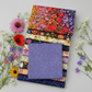 Dotty Thatched Periwinkle fabric by Robin Pickens for Moda Fabrics — periwinkle-blue with scattered tonal dots — shown beside a coordinating stack of Superbloom quilting cotton fabrics by Robin Pickens for Moda Fabrics with vibrant botanical florals. 100% cotton, 43–44" wide. Coordinating fabrics and quilt patterns available at IraRobi Quilts.
