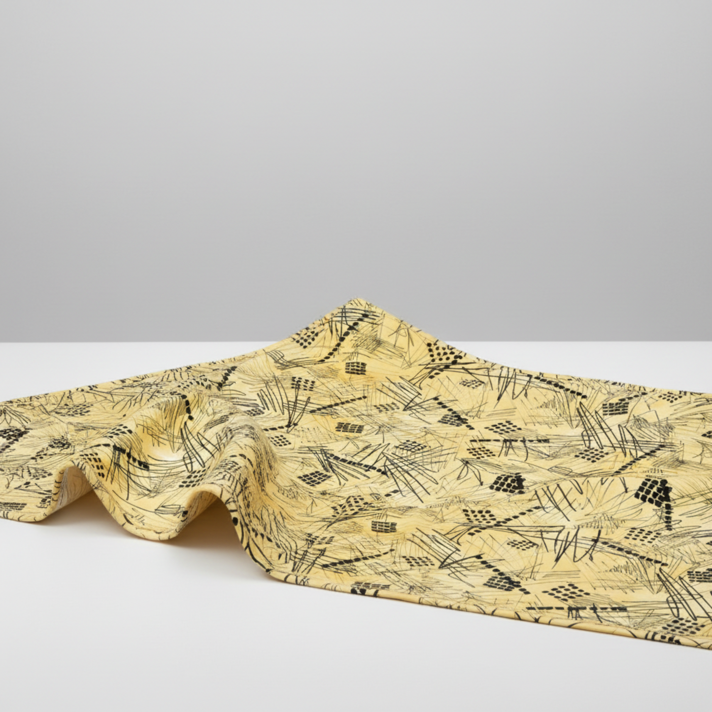 Heat Wave Bask Sun quilting cotton draped on light grey surface — bold black abstract scratch lines and grid squares on golden yellow ground by Katie Pasquini Masopust for FreeSpirit Fabrics