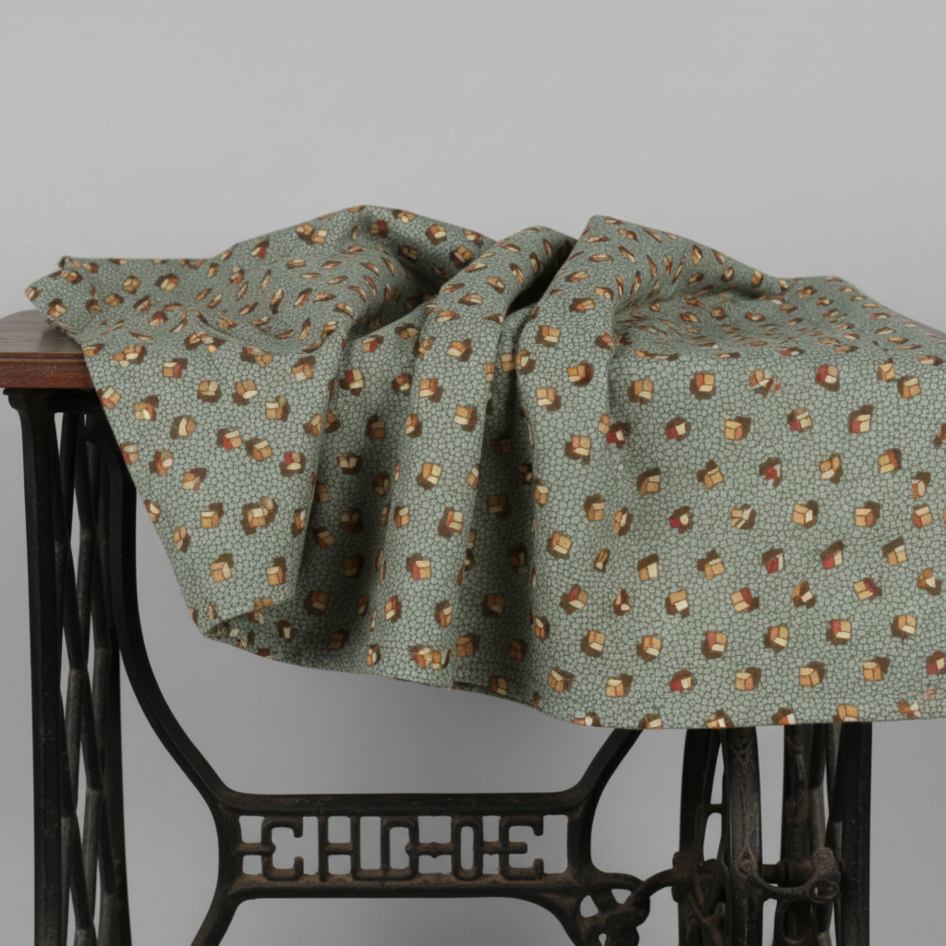 The Fox Homestead Slate Blue Green Tossed Cubes quilting cotton by Stacy West for Henry Glass — fabric draped over an antique sewing machine showing softness and natural drape