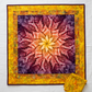 Medallion quilt featuring the Dream Big Leaf Mulberry panel by Jeanie Sumrall-Ajero for Hoffman Fabrics as the center – leaf mandala radiating from a glowing golden yellow center through warm peach-orange to rich pink and deep purple-plum outer leaves, surrounded by a scrappy pieced border of Expressions Batiks Hand-Dyes Yellow Orange Multi III by Riley Blake Designs in golden yellow, warm orange, chartreuse green, olive, and amber, finished with a deep plum binding, with folded Yellow Orange Multi III bati