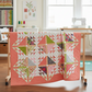 Dotty Thatched Carnation quilting cotton by Robin Pickens for Moda Fabrics — shown in the Emilia Quilt Pattern by Robin Pickens displayed on a quilt rack in a bright quilting studio with coordinating Superbloom florals in pinks, greens, and creams. Quilts shown for inspiration feature the Emilia Quilt Pattern by Robin Pickens — available at IraRobi Quilts.