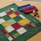 Nature-inspired jewel-tone quilt flat lay featuring Expressions Batiks Hand-Dyes Evergreen by Riley Blake Designs as the background fabric – rich deep forest green hand-dyed batik with organic mottled texture in pieced blocks with coordinating warm red, golden yellow, soft sage, and cream tonal batiks, folded fabric swatches on a warm linen surface