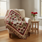 Finished Sonata quilt in Everlasting Rose fabrics draped over a cream armchair with red roses on side table – cozy home setting showing crimson, sage green and cream medallion design