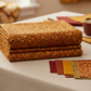 Falling Leaves Multi Diamond Leaves fabric by Jason Yenter for In The Beginning Fabrics folded on a linen surface – dark brown leaf sprigs cascading over diamond geometric grid in rich burnt orange, amber, and golden autumn tones, perfect for cozy fall quilt projects, 100% cotton, 3 yard cut