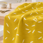 Filigree Rice Saffron fabric by Zen Chic for Moda Fabrics draped over a wooden sewing table in a bright studio with pins, thread, and scissors. Available at IraRobi Quilts.