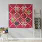 Fiona's Daisy Chain quilt pattern by Robin Pickens made with Thatched Fuchsia fabric by Robin Pickens for Moda Fabrics — bright fuchsia-hot pink tonal crosshatch background with cream nine-patch cross blocks and dark botanical floral print squares, displayed on a grey wall with a wooden ladder and stool. Quilt pattern and coordinating fabrics available at IraRobi Quilts.