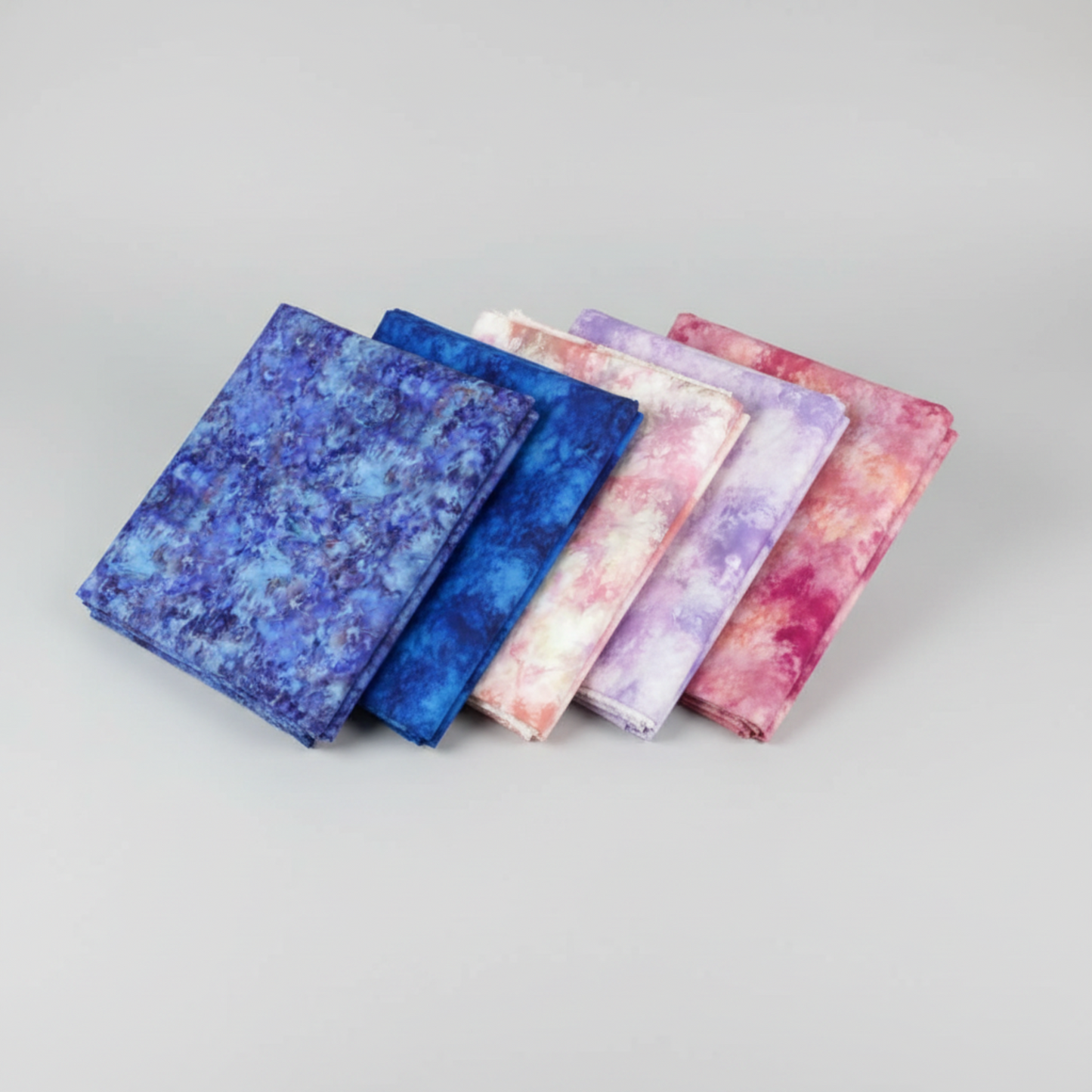 Fire & Ice by Maywood Studio cotton quilting fabric collection showing Navy, Royal Blue, Blush, Lavender, and Berry Ice Dye colorways folded and fanned on light grey background