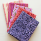 Five folded Superbloom fabrics by Robin Pickens for Moda Fabrics arranged in a fan, featuring Leafy Indigo, Leafy Geranium, Daisyish Freesia, and Orchid and Cream Scribble Stripes.