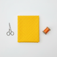 Yellow quilting cotton fabric with orange polka dots, folded flat with fabric scissors and orange thread spool on light grey background — IraRobi Quilts