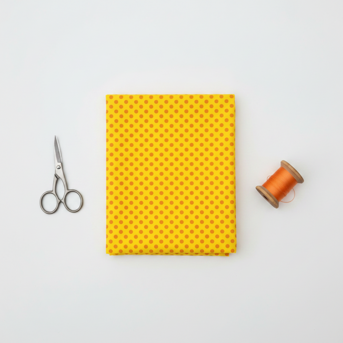Yellow quilting cotton fabric with orange polka dots, folded flat with fabric scissors and orange thread spool on light grey background — IraRobi Quilts
