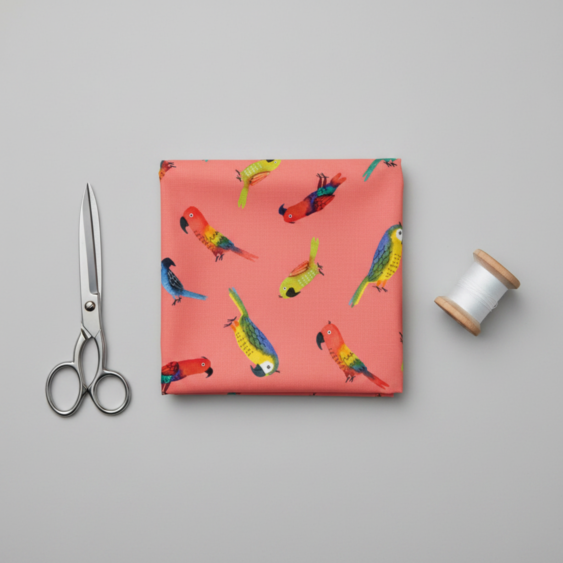 Safari Fun Jungle Birds Sorbet quilting fabric folded flat with fabric scissors and thread spool on light grey background — coral parrot print by Terry Runyan for Benartex