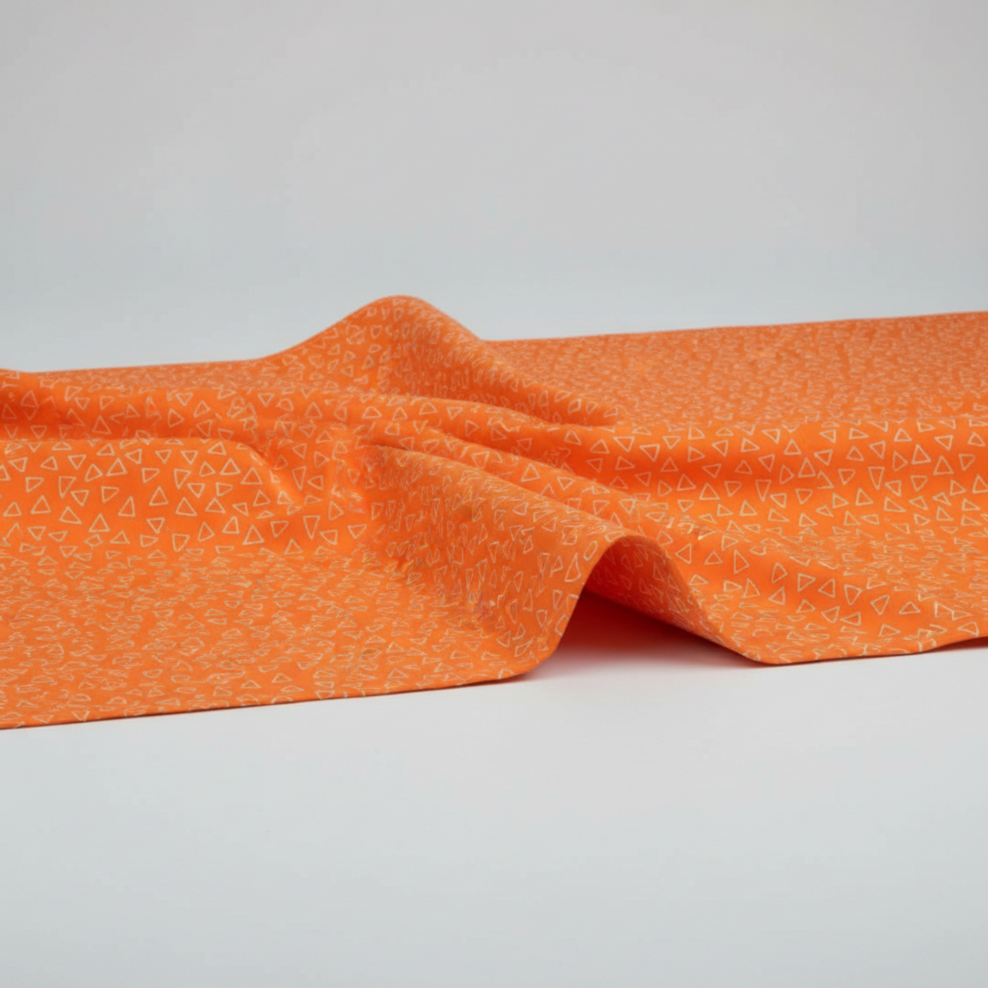 Safari Fun Floating Triangles Orange by Terry Runyan for Benartex – fabric softly draped showing hand and weight of the quilting cotton, light grey background