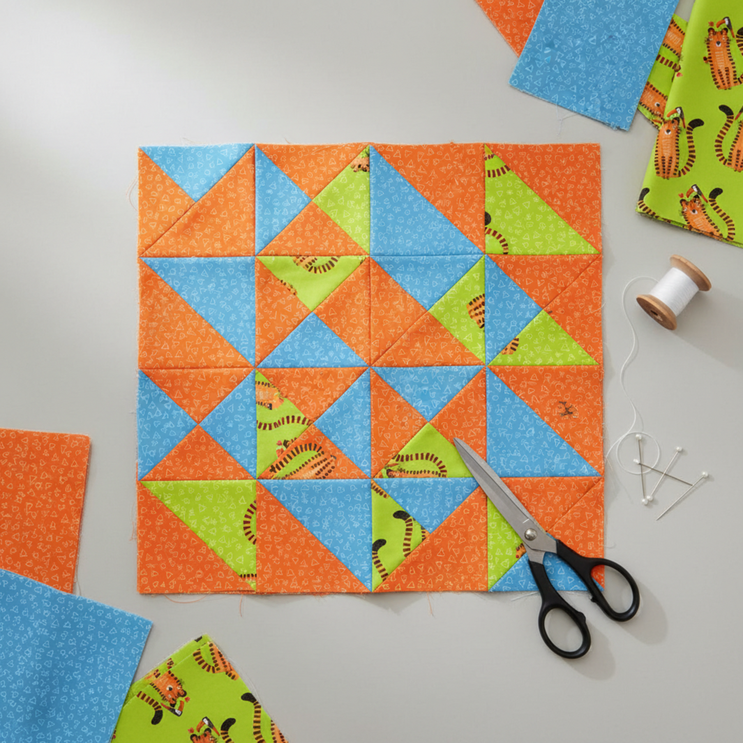 Safari Fun Floating Triangles Orange by Terry Runyan for Benartex – half-square triangle quilt blocks in progress with coordinating blue and green Safari Fun fabrics, scissors and thread