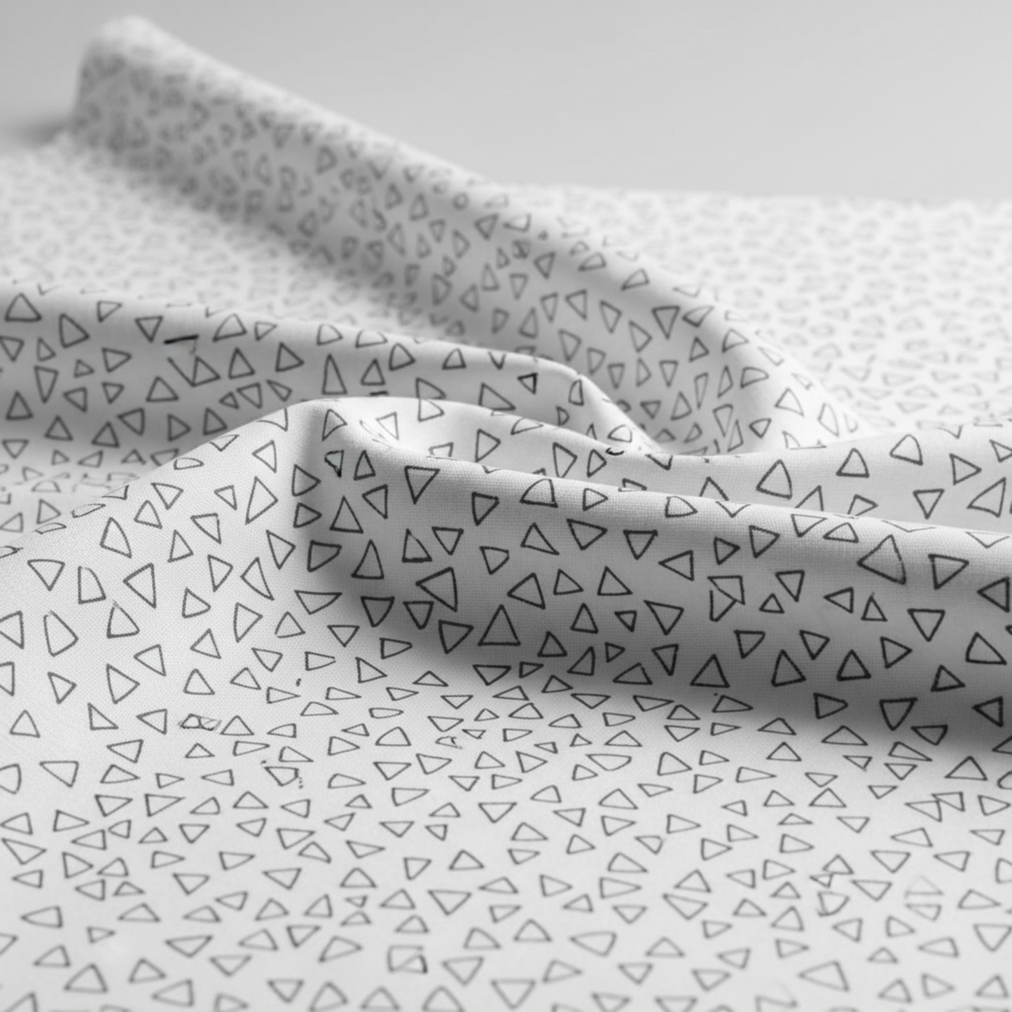 Safari Fun Floating Triangles White/Black by Terry Runyan for Benartex – close-up of fabric draped softly showing hand and weight of the quilting cotton with scattered black hand-drawn triangle outlines