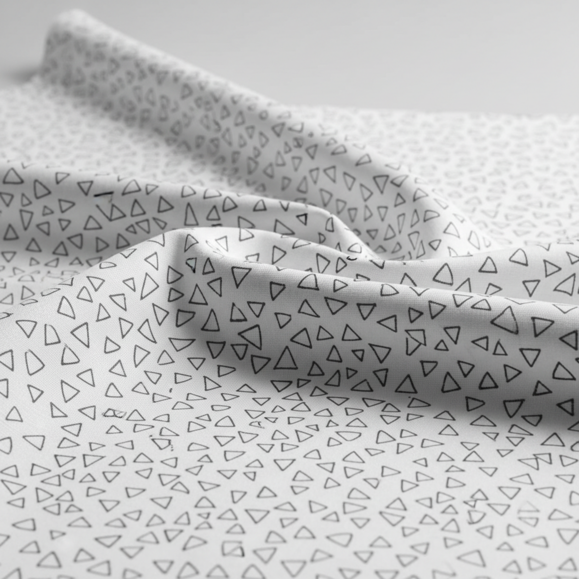 Safari Fun Floating Triangles White/Black by Terry Runyan for Benartex – close-up of fabric draped softly showing hand and weight of the quilting cotton with scattered black hand-drawn triangle outlines