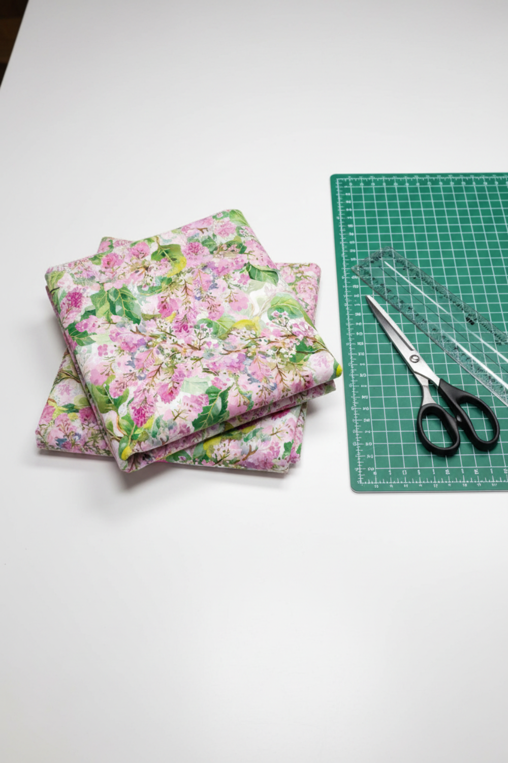 Folded Decoupage Pink Lilac quilting fabric beside a green cutting mat, clear ruler, and fabric scissors.