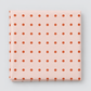 Frisky In A Row Sweetie fabric by Zen Chic for Moda Fabrics, neatly folded on a light grey background, showing neat rows of rust-orange dots on a soft blush-pink ground.