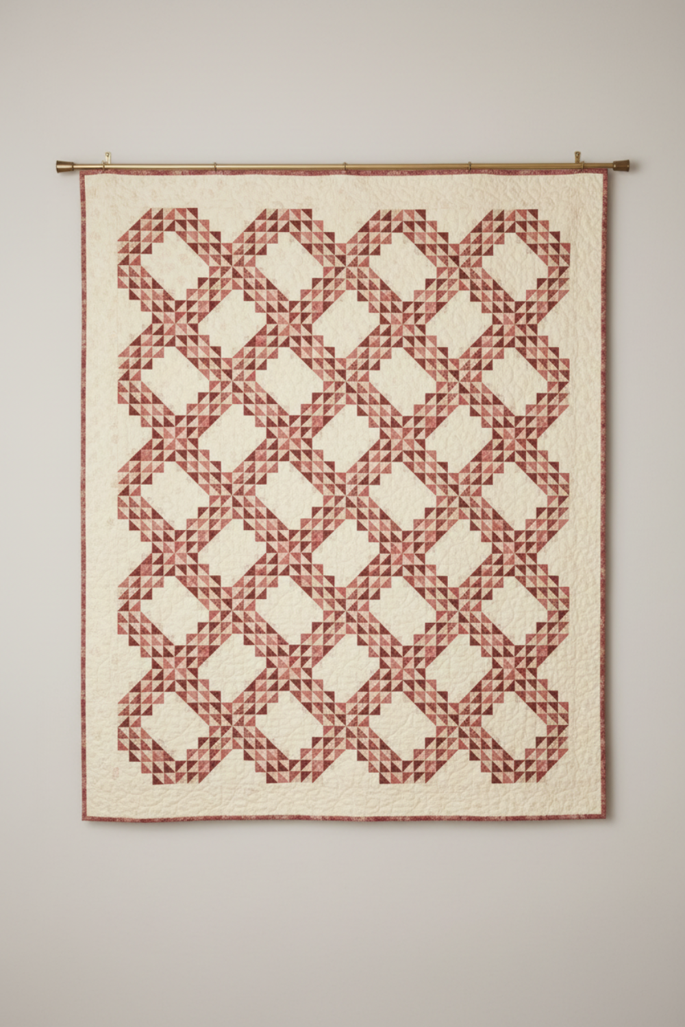 Fox Homestead Pink Leaves and Berries fabric by Stacy West for Henry Glass — quilt shown for inspiration features an interlocking geometric block pattern in dusty rose, muted burgundy, and olive-khaki tones on a warm cream background, displayed on a wall.