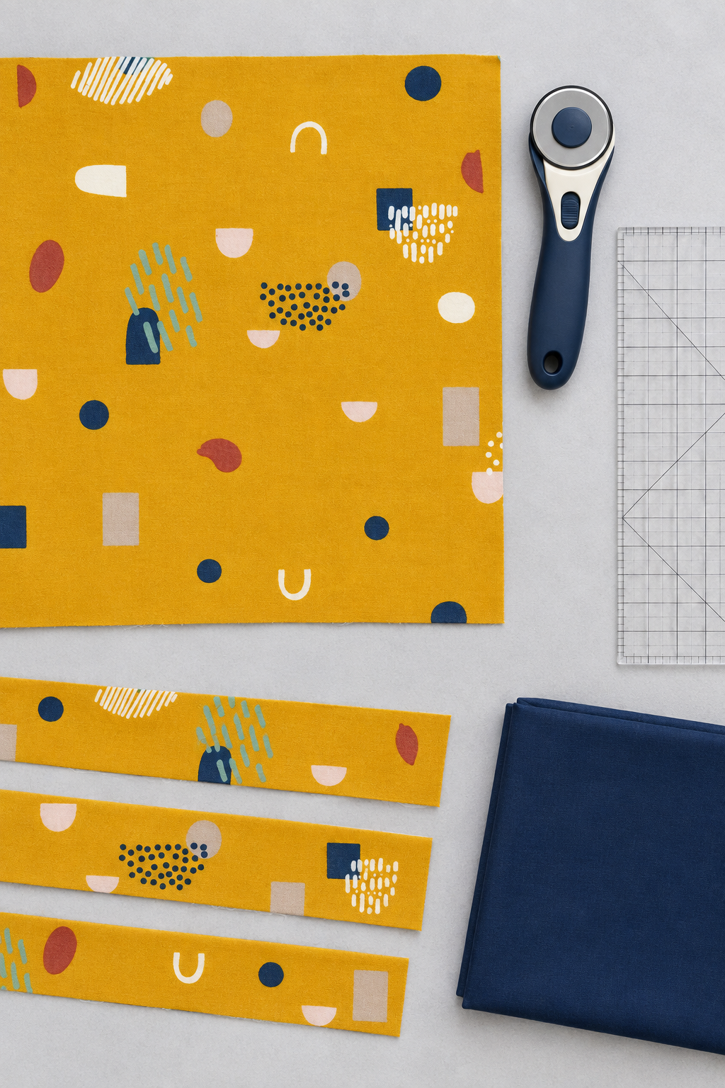 Frisky Catch Me Sunny fabric by Zen Chic for Moda Fabrics laid flat with cut strips, a rotary cutter, a clear quilting ruler, and a folded navy coordinating fabric. Available at IraRobi Quilts.