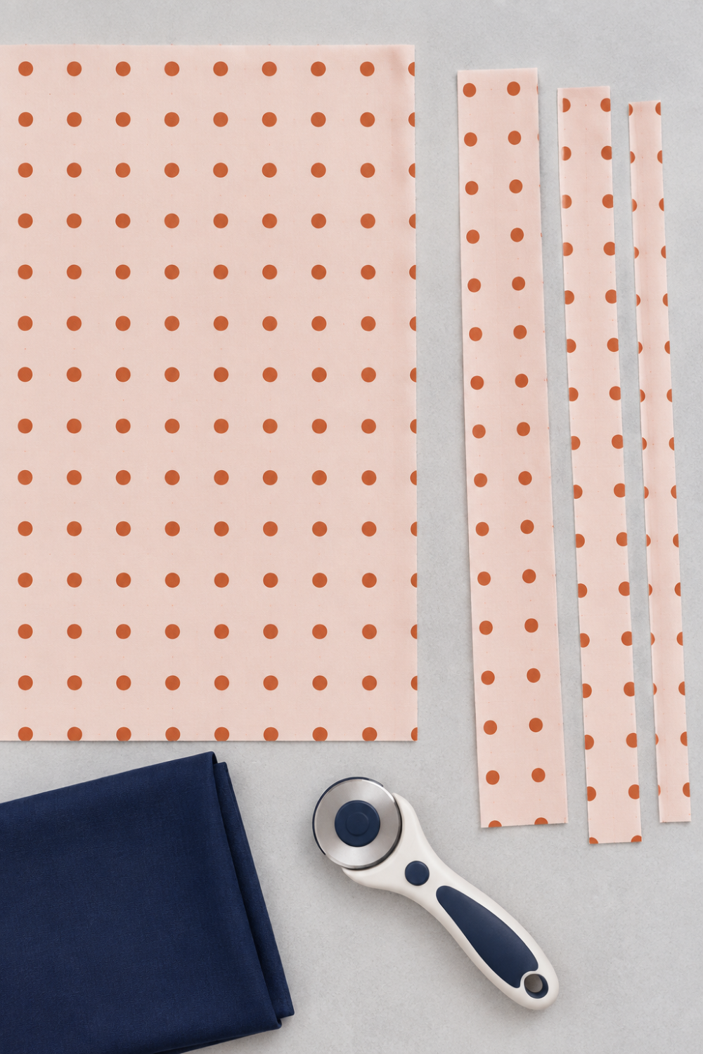 Frisky In A Row Sweetie fabric by Zen Chic for Moda Fabrics laid flat with cut strips, a rotary cutter, and a folded navy coordinating fabric. Available at IraRobi Quilts.