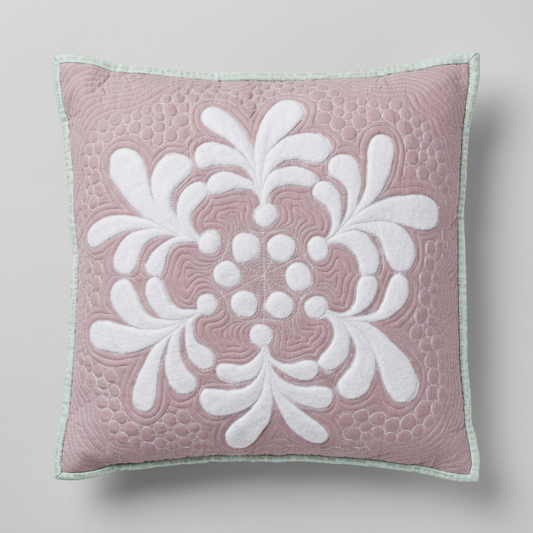 Frosted Blooms dusty-mauve quilted pillow with raised white floral motifs, pebble quilting, and pale mint edging on a light grey background.