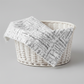 Writing on the Wall Going Places White quilting cotton by Sew Kind of Wonderful for FreeSpirit Fabrics -- fabric draped over a white wicker basket on a light grey surface, crisp white ground with handwritten black travel words including Travel, New Places, Joy, Ocean, Waves, Beach, Sunshine, and Create