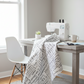 Writing on the Wall Going Places White quilting cotton by Sew Kind of Wonderful for FreeSpirit Fabrics -- bright airy sewing room lifestyle scene with white travel word fabric draped over a sewing chair and table, modern white sewing machine, thread spools, scissors, potted plant, paper map, and ceramic mug in natural light