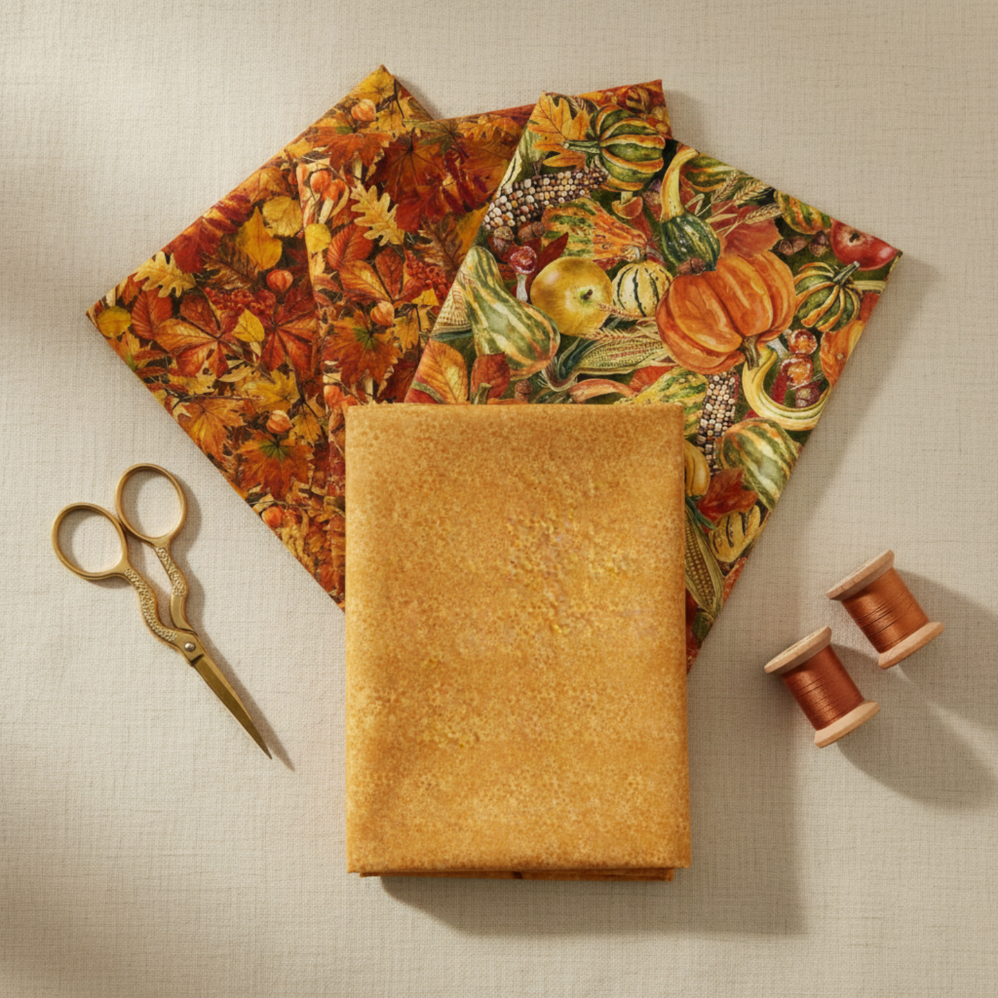 Autumn Celebration Gold Berries quilting cotton — folded fat quarter as front hero with coordinating Autumn Celebration autumn leaf and Multi Vegetables harvest prints fanned behind. Brass scissors and amber thread spools on cream linen. Coordinating fabrics and quilt patterns available at IraRobi Quilts.