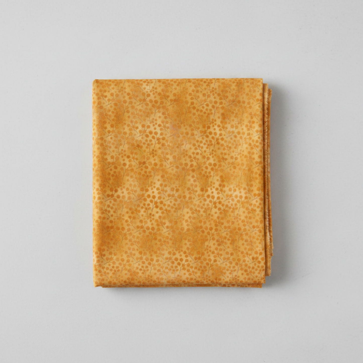 Autumn Celebration Gold Berries quilting cotton — neatly folded fat quarter on a light grey surface showing scattered amber dot clusters in loose groupings on a mottled golden amber ground. Selvage edge visible on the right. Low-contrast tonal blender. 100% cotton, 43–44" wide.