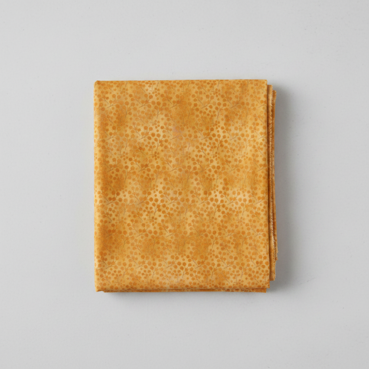Autumn Celebration Gold Berries quilting cotton — neatly folded fat quarter on a light grey surface showing scattered amber dot clusters in loose groupings on a mottled golden amber ground. Selvage edge visible on the right. Low-contrast tonal blender. 100% cotton, 43–44" wide.