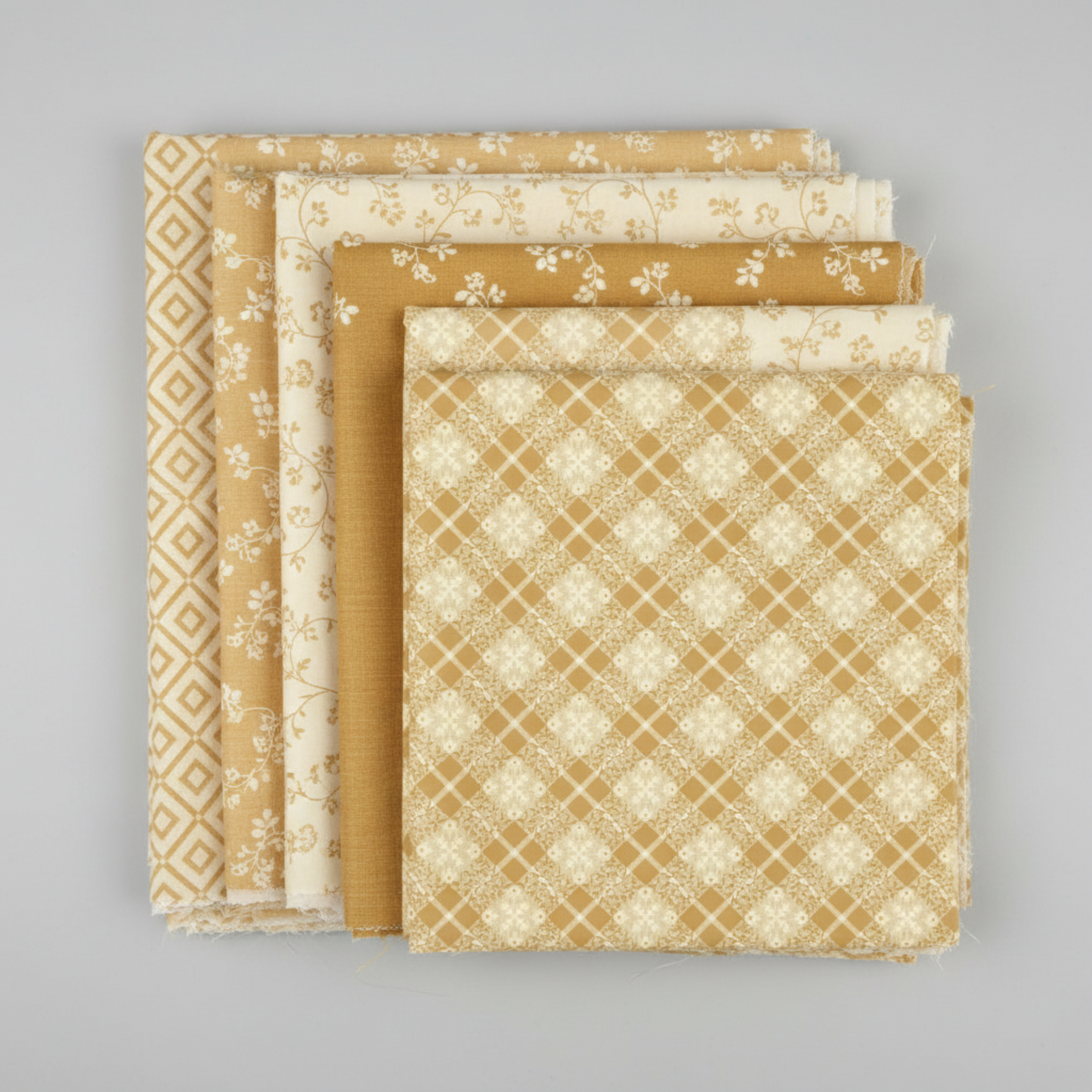 Golden Era quilting cotton collection by Paula Barnes for Marcus Fabrics — coordination stack of five tan-gold and cream tonal blender fabrics fanned on light grey background, including diagonal lattice, small florals, near-solid, and vine prints