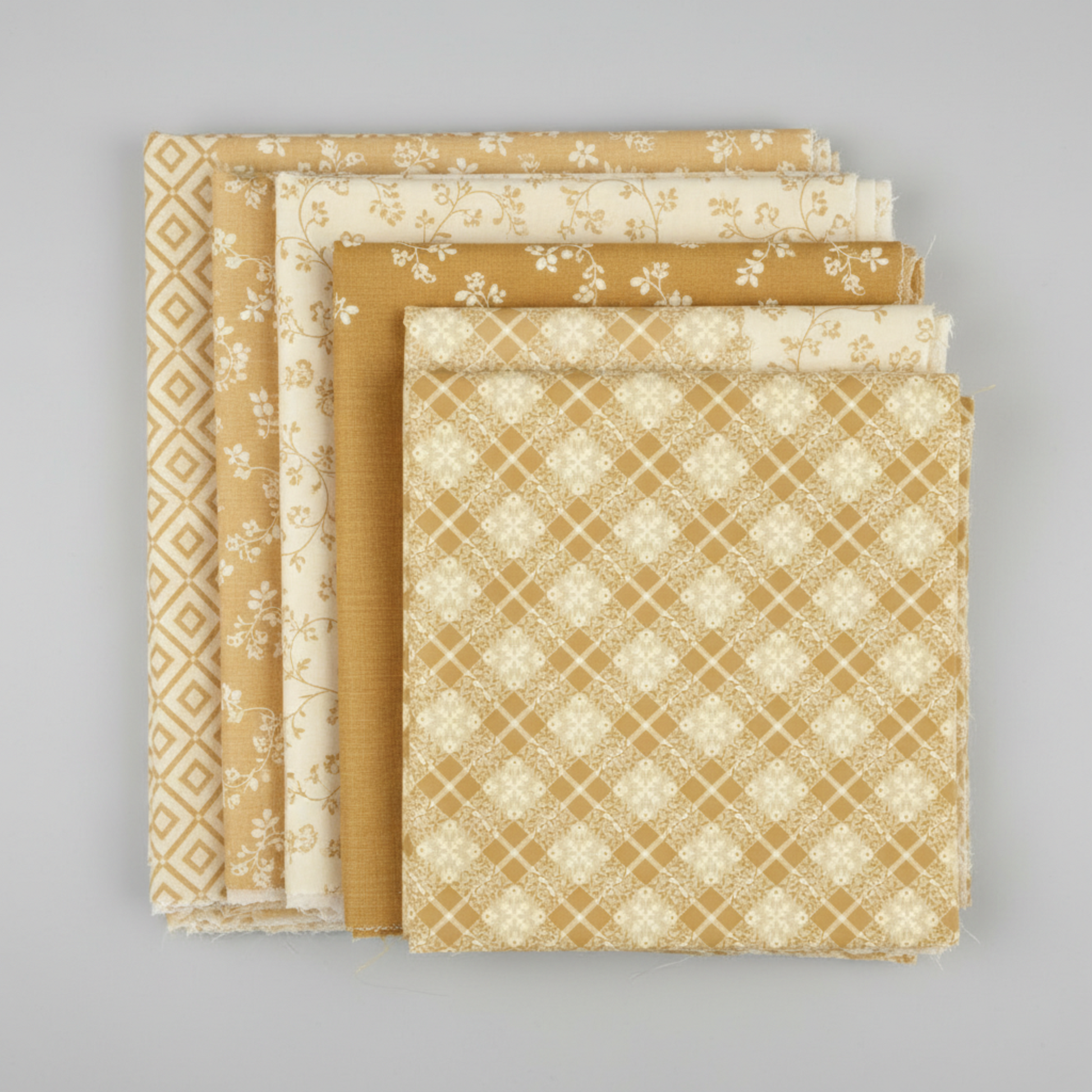 Golden Era quilting cotton collection by Paula Barnes for Marcus Fabrics — coordination stack of five tan-gold and cream tonal blender fabrics fanned on light grey background, including diagonal lattice, small florals, near-solid, and vine prints