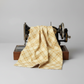 GGolden Era Floral Plaid Tan quilting cotton by Paula Barnes for Marcus Fabrics — fabric draped over a vintage sewing machine showing natural folds, warm tan-gold ground with diagonal lattice grid and delicate cream floral wreath motifs