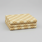 Golden Era Floral Plaid Tan quilting cotton by Paula Barnes for Marcus Fabrics — three folded yards stacked on a grey surface, warm tan-gold diagonal lattice with cream floral wreath motifs in each diamond cell