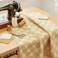 Golden Era Floral Plaid Tan quilting cotton by Paula Barnes for Marcus Fabrics — styled sewing room flat lay in warm traditional aesthetic with tan-gold lattice fabric, vintage sewing machine, gold thread spools, scissors, and coordinating cream and tan fabric swatches