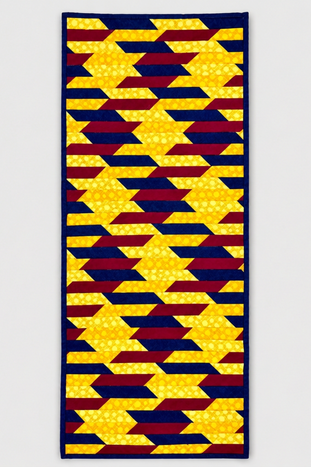 Golden Weave handmade quilted table runner with golden yellow dotted fabric, interlacing navy and burgundy strips, and navy binding, displayed flat on light gray.