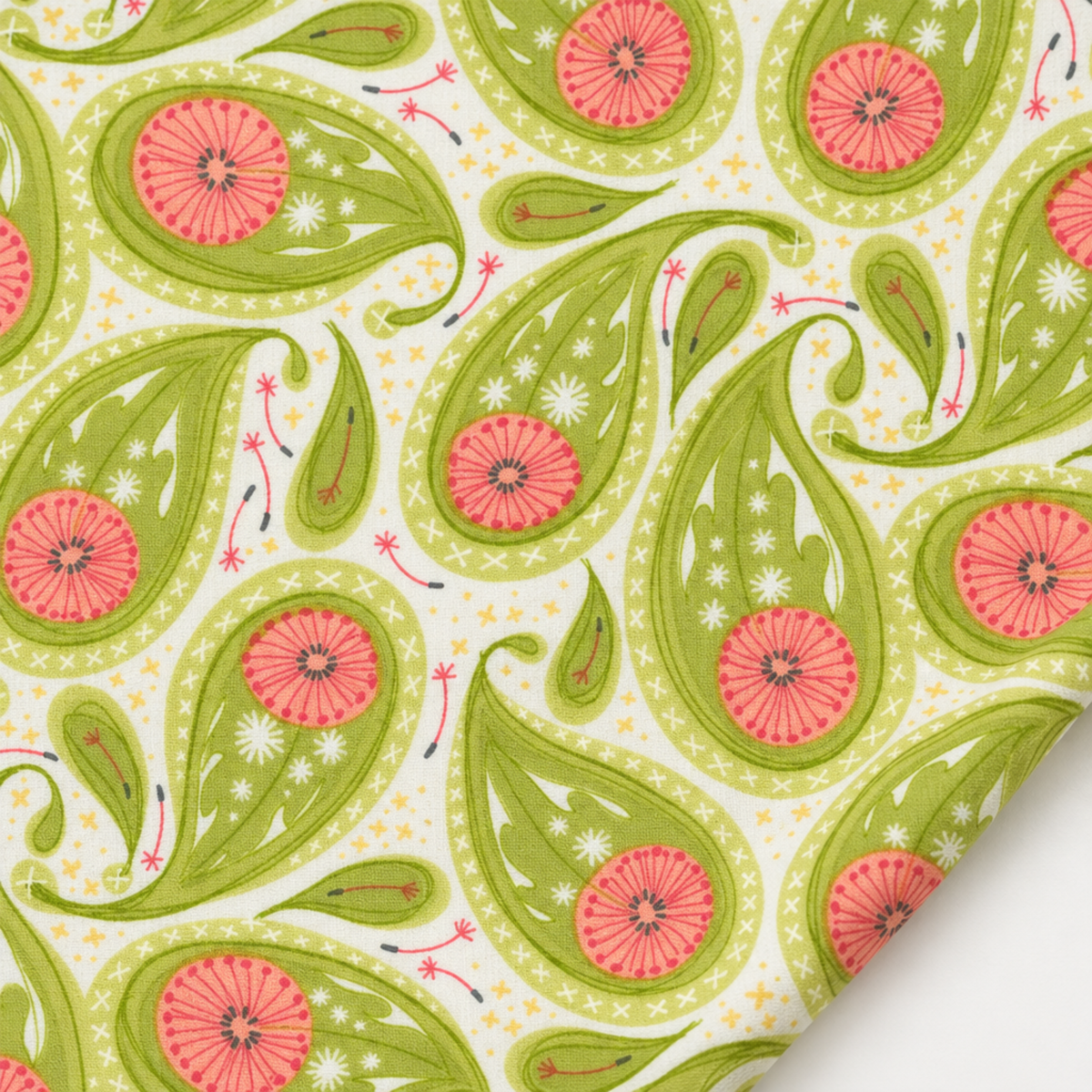 Dandi Duo Grass fabric laid flat with one folded corner, showing its green paisley and coral-pink floral print.