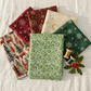 Winter Solstice II Green on White Snow Swirl Fabric by Jason Yenter for In The Beginning Fabrics — shown with coordinating quilting cottons fanned flat, with green and gold thread spools and a holly sprig. Coordinating fabrics and quilt patterns are available at IraRobi Quilts.
