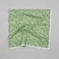 Winter Solstice II Green on White Snow Swirl quilting cotton by Jason Yenter for In The Beginning Fabrics — fabric draped over a grey surface showing natural folds and raw cut edge, flowing white scroll swirls with snowflakes and stars on mottled watercolor green. Quilt blocks shown for inspiration. Coordinating fabrics and quilt patterns are available at IraRobi Quilts.