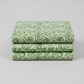 Winter Solstice II Green on White Snow Swirl quilting cotton by Jason Yenter for In The Beginning Fabrics — three folded yards stacked on a grey surface showing flowing white scroll swirls with snowflakes and scattered stars on mottled watercolor green. Quilt blocks shown for inspiration. Coordinating fabrics and quilt patterns are available at IraRobi Quilts.