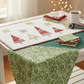 Winter Solstice II Green on White Snow Swirl Fabric by Jason Yenter for In The Beginning Fabrics — shown as the green tree fabric in the Snowy Pines Table Runner by Margot Languedoc, cozy sewing room work in progress with fairy lights. Quilts shown for inspiration feature the Snowy Pines Table Runner by Margot Languedoc for The Pattern Basket — available at IraRobi Quilts.