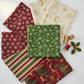 Five fabrics fanned flat featuring green snowflakes metallic, crimson snowflakes metallic, cream celestial metallic, multi stripe metallic, and multi deer metallic, with gold and red thread spools and holly sprig. Quilt blocks shown for inspiration. Coordinating fabrics and quilt patterns are available at IraRobi Quilts.