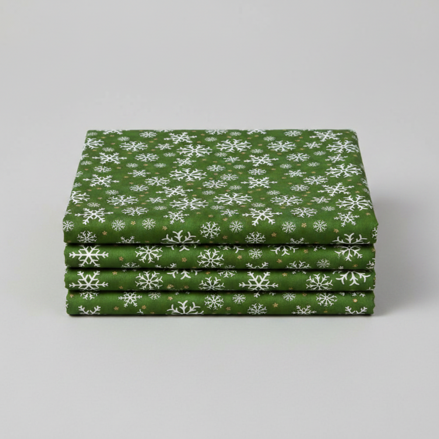 Winter Solstice II Green Snowflakes Metallic quilting cotton by Jason Yenter for In The Beginning Fabrics — three folded yards stacked on a grey surface showing rich deep forest green ground with tossed white snowflakes and gold metallic star dots. Quilt blocks shown for inspiration. Coordinating fabrics and quilt patterns are available at IraRobi Quilts.